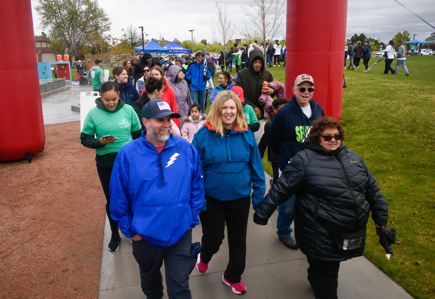People walking through a park under a large red and white arch for the NAMI Walks event.