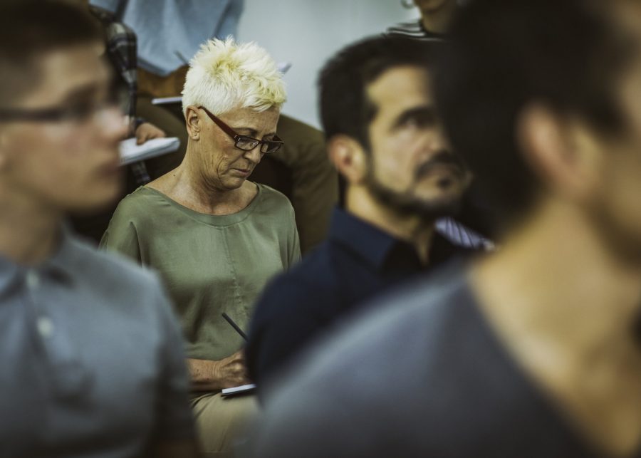 A woman with white hair sits in the audience, surrounded by a group of individuals.